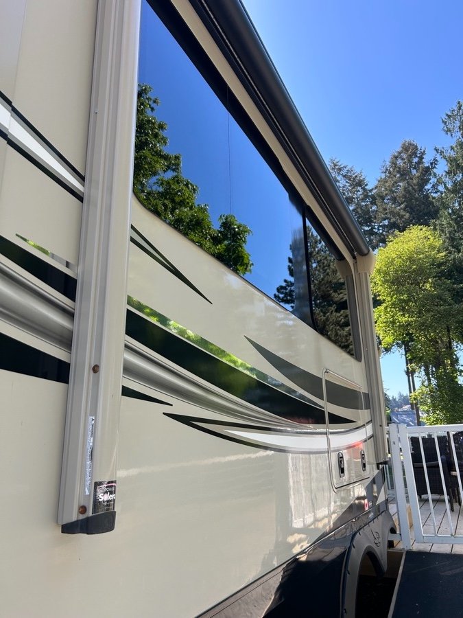 Freshly detailed RV exterior with a mirror-like shine, reflecting trees and sky